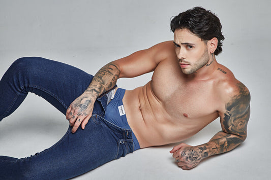 **Tattooed man posing shirtless in jeans and underwear.**
